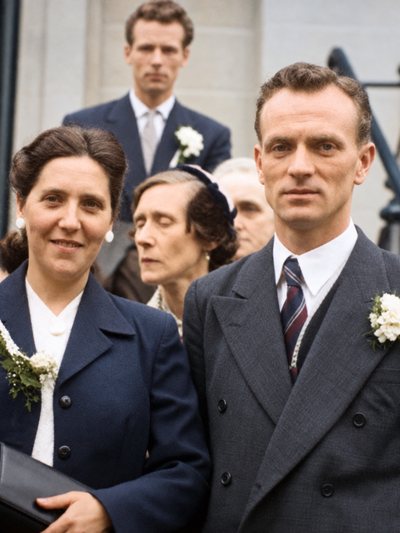 A couple wearing wedding buttonholes on church steps, guests behind them.